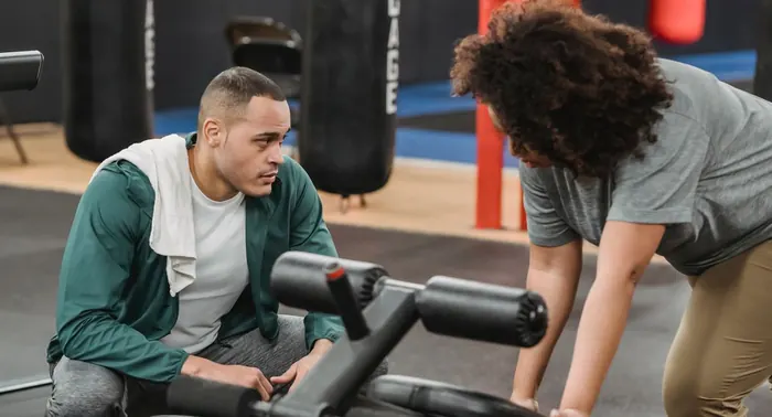 Instrutor acompanha mulher fazendo exercício em banco de treino com saco de pancada ao fundo