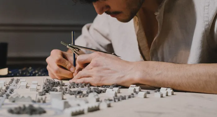 Arquiteto desenhando com compasso sobre maquete de projeto urbanístico