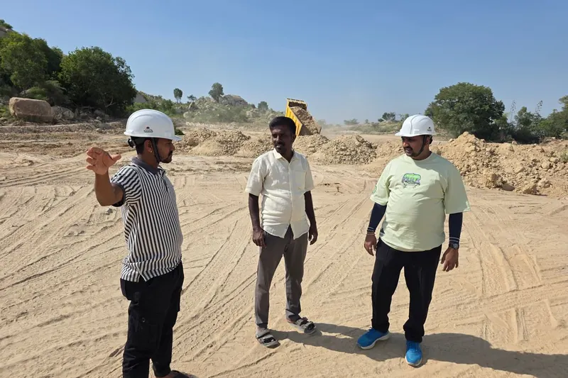 Três engenheiros de capacete conversando em um terreno de obra com máquinas ao fundo.