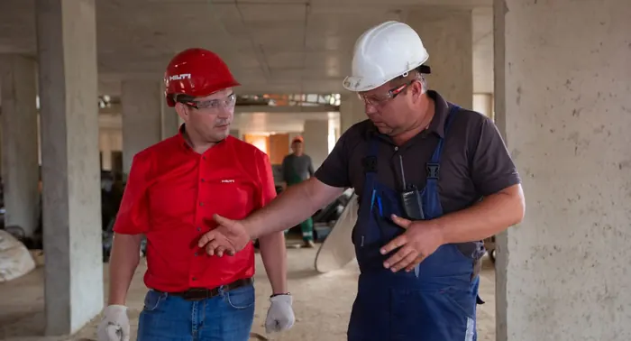 Dois trabalhadores de capacete conversando em estrutura de concreto em obra