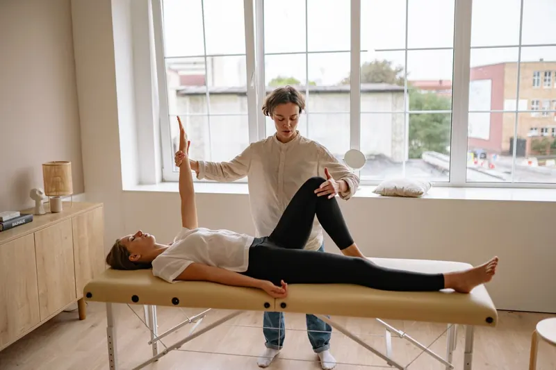 Fisioterapeuta orientando paciente em exercício de reabilitação, com maca e bolas terapêuticas ao fundo
