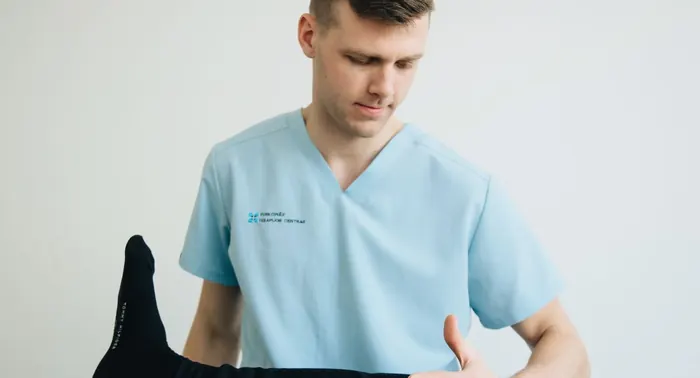 Fisioterapeuta de uniforme azul-claro conduzindo exercício de alongamento da perna de um paciente