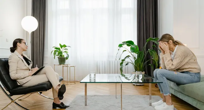 Psicóloga com caderno sentada em poltrona diante de paciente, em sala clara com plantas