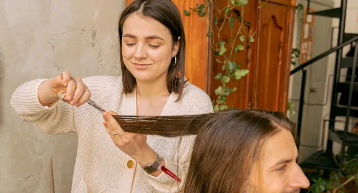 Profissional cortando com tesoura e pente os cabelos longos de um cliente em salão