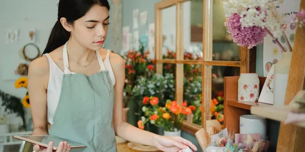 Florista de avental usando um tablet em meio aos arranjos de sua loja de flores