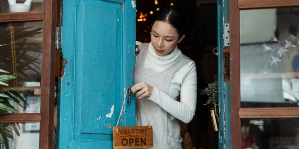 Mulher virando a placa de aberto na porta de madeira azul de uma cafeteria