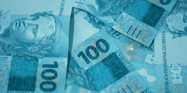 Cédulas de cem reais espalhadas formando um fundo azul