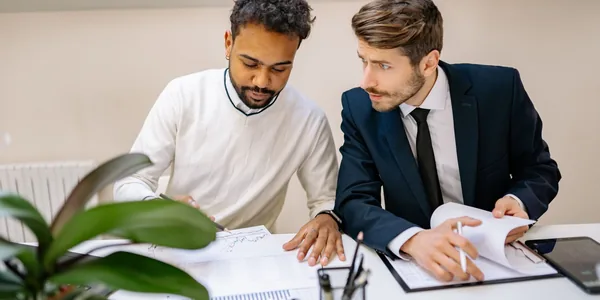Dois profissionais analisando documentos com gráficos sobre a mesa de um escritório