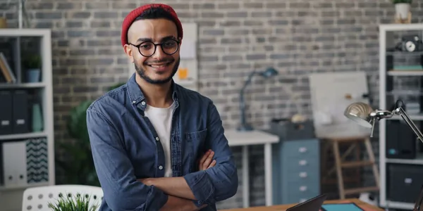 Jovem empresário de braços cruzados e sorrindo em um escritório de parede de tijolos