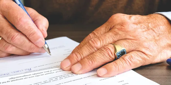 Close das mãos de uma pessoa assinando um documento sobre a mesa
