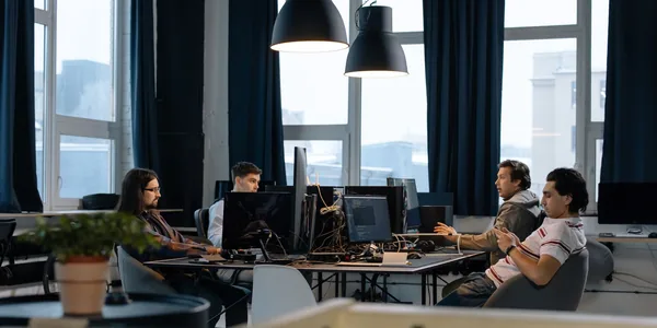 Escritório de empresa de tecnologia com bancadas compartilhadas, computadores e luminárias suspensas