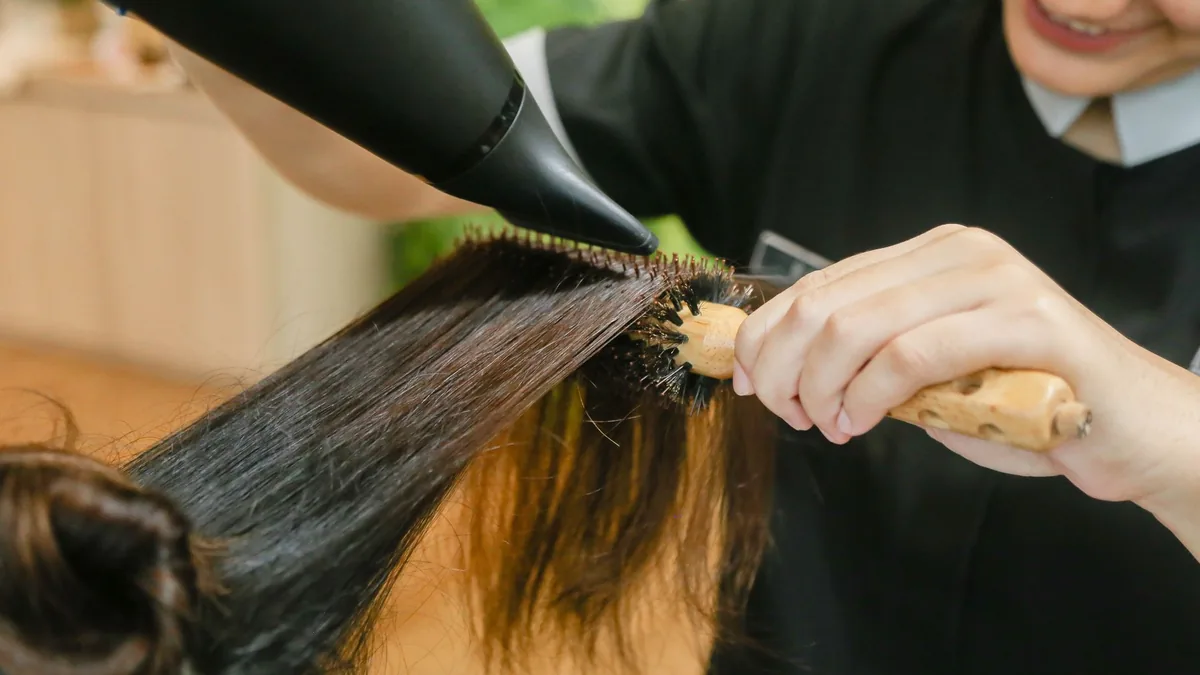 Close de cabeleireira finalizando a escova de uma cliente com secador e escova redonda