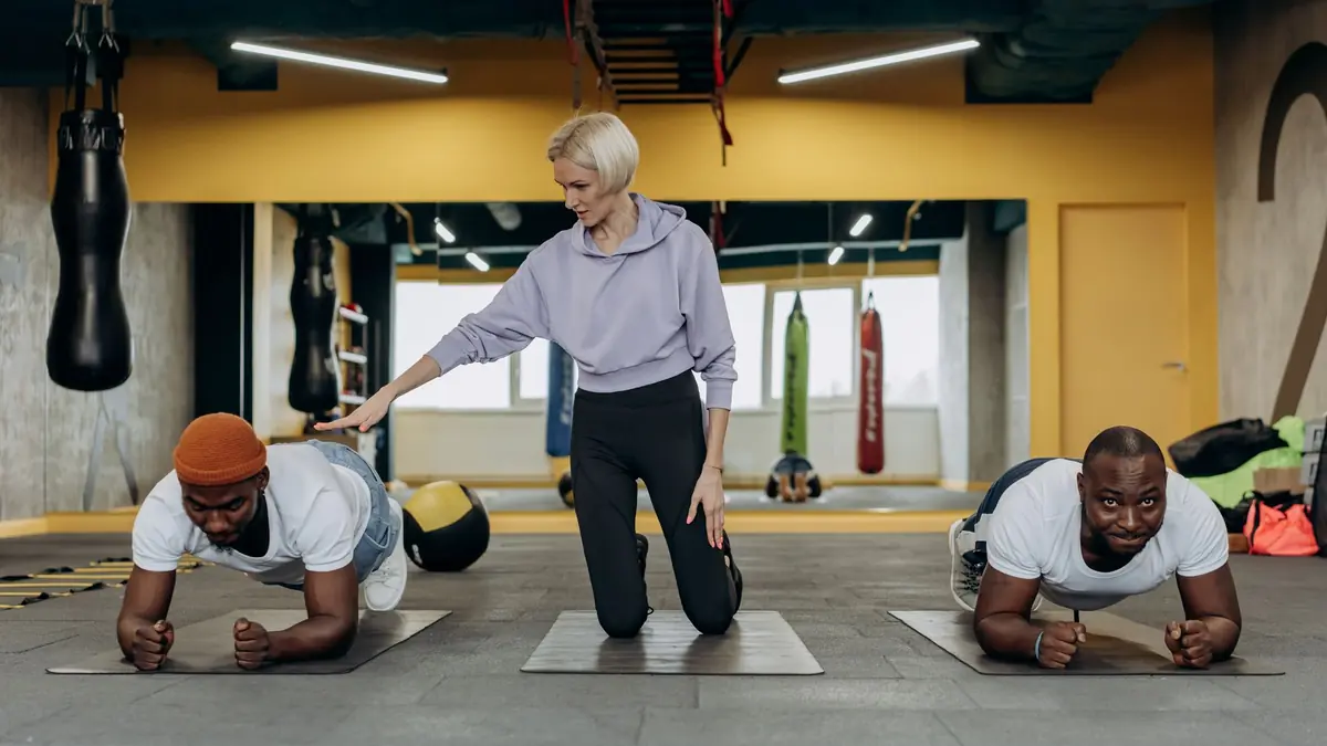 Professor orientando dois alunos em exercício de solo dentro de um box de treino.
