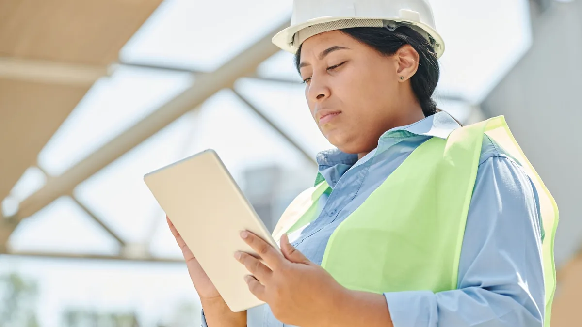 Engenheira de capacete e colete conferindo informações em um tablet no canteiro de obras.