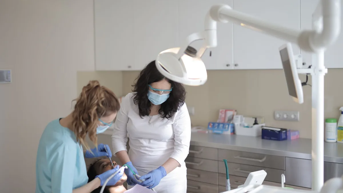Dentista e auxiliar atendendo um paciente na cadeira do consultório odontológico.