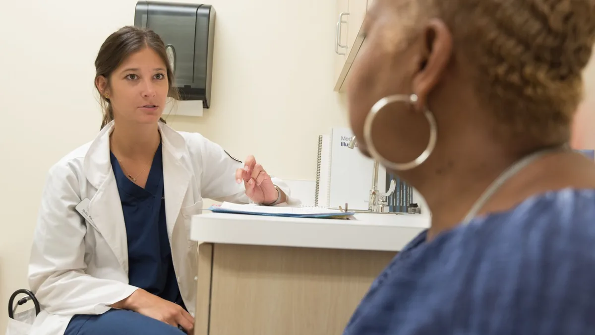 Profissional de jaleco branco conversando com uma paciente no balcão do consultório.