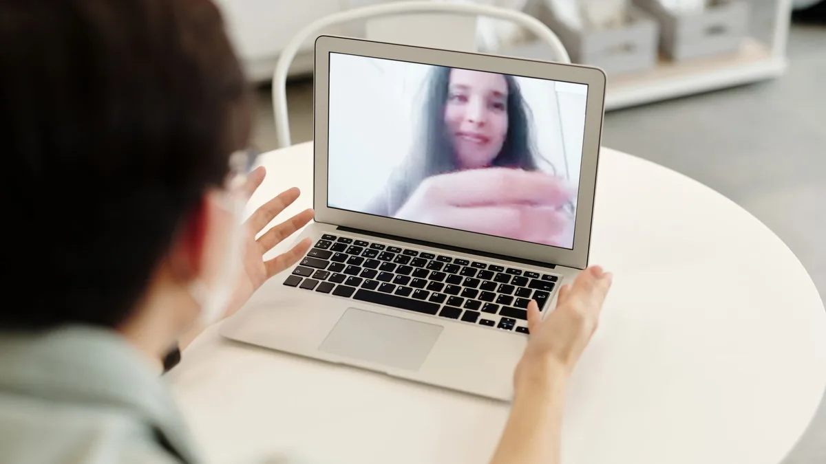 Pessoa em atendimento por videochamada no notebook, sobre uma mesa clara.