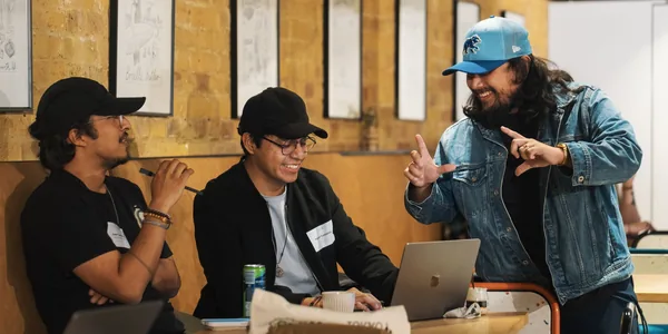 Três profissionais de criação conversando em volta de uma mesa com um notebook aberto.