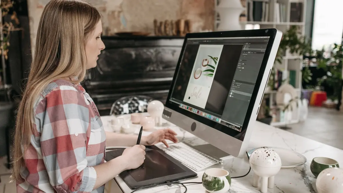 Designer editando uma arte na mesa digitalizadora em frente a dois monitores.