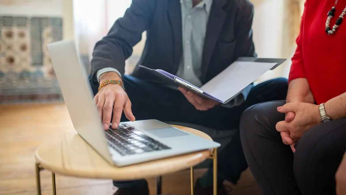 Consultores analisando documentos e um notebook durante a reunião com o cliente.