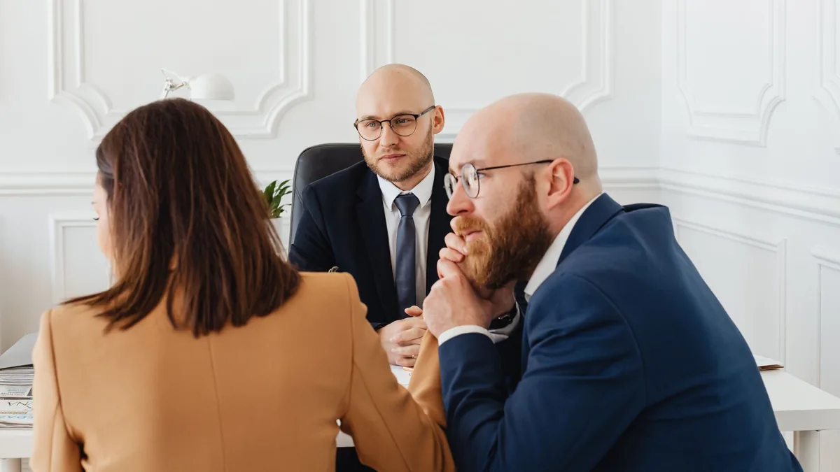 Consultor conversando com dois clientes em volta da mesa de reunião.
