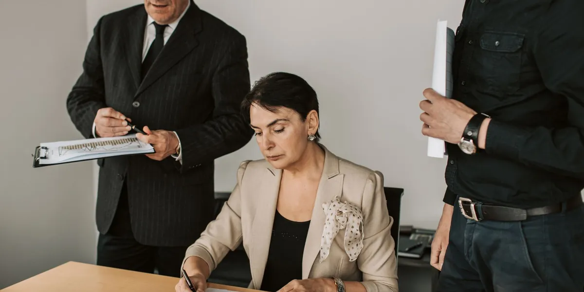 Três profissionais reunidos em volta de uma mesa de escritório analisando documentos financeiros impressos.