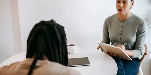 Profissional anotando em uma prancheta durante um atendimento, com a paciente de costas para a câmera.