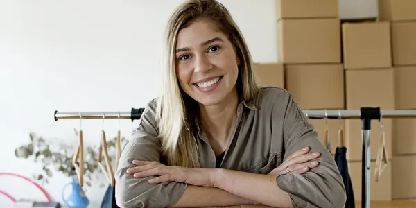 Lojista sorrindo enquanto organiza encomendas ao lado de uma arara de roupas