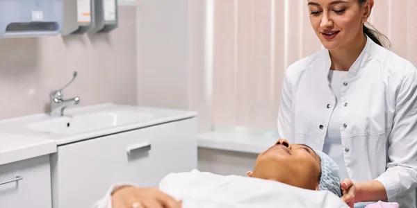 Profissional de est&eacute;tica atendendo uma cliente em uma sala clara de cl&iacute;nica