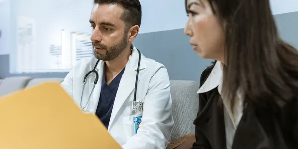 M&eacute;dico mostrando uma pasta de documentos para uma pessoa em um consult&oacute;rio