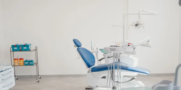 Consult&oacute;rio odontol&oacute;gico claro com cadeira azul e equipamentos