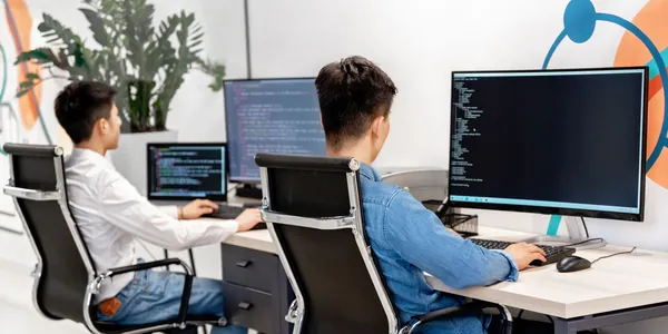 Dois desenvolvedores trabalhando em monitores com c&oacute;digo em um escrit&oacute;rio claro