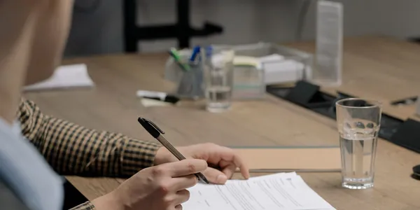 Profissional assinando um documento sobre a mesa de reuni&atilde;o de um escrit&oacute;rio
