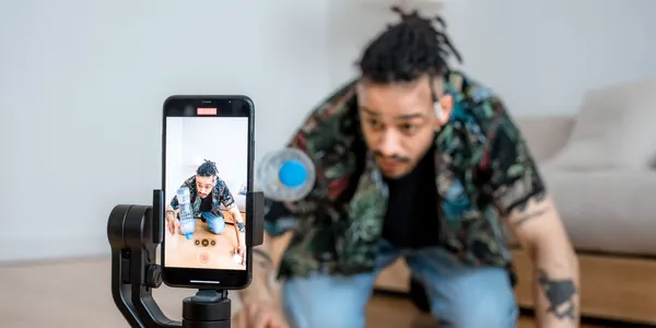 Criador de conte&uacute;do sendo filmado por um celular em estabilizador dentro de casa