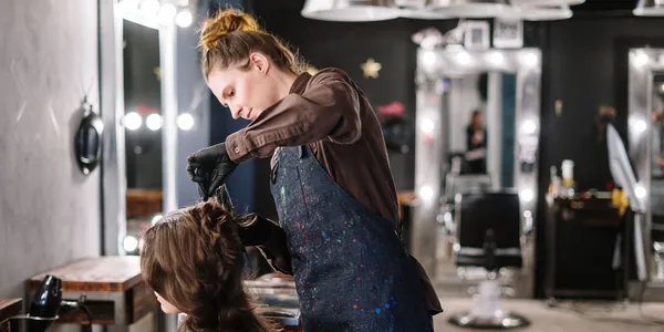 Cabeleireira finalizando o cabelo de uma cliente em um sal&atilde;o com espelhos iluminados