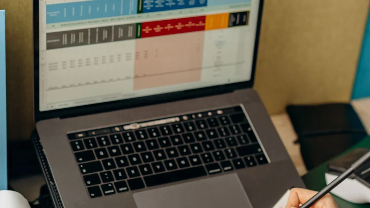Mãos anotando observações em um caderno ao lado do notebook com relatórios abertos