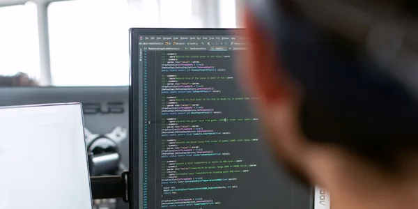 Desenvolvedor sentado diante do monitor com linhas de código na tela