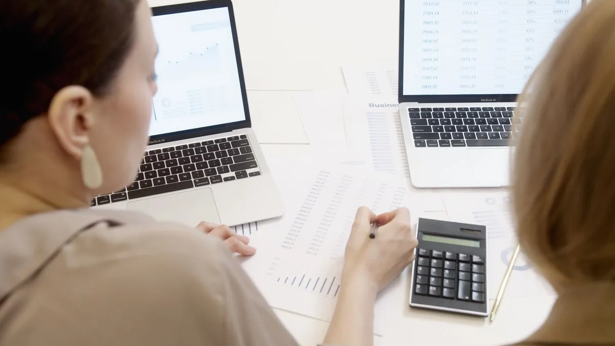 Duas pessoas comparando dados em notebooks abertos sobre a mesa