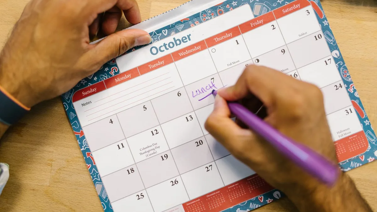Mão marcando uma data no calendário de mesa aberto no mês de outubro