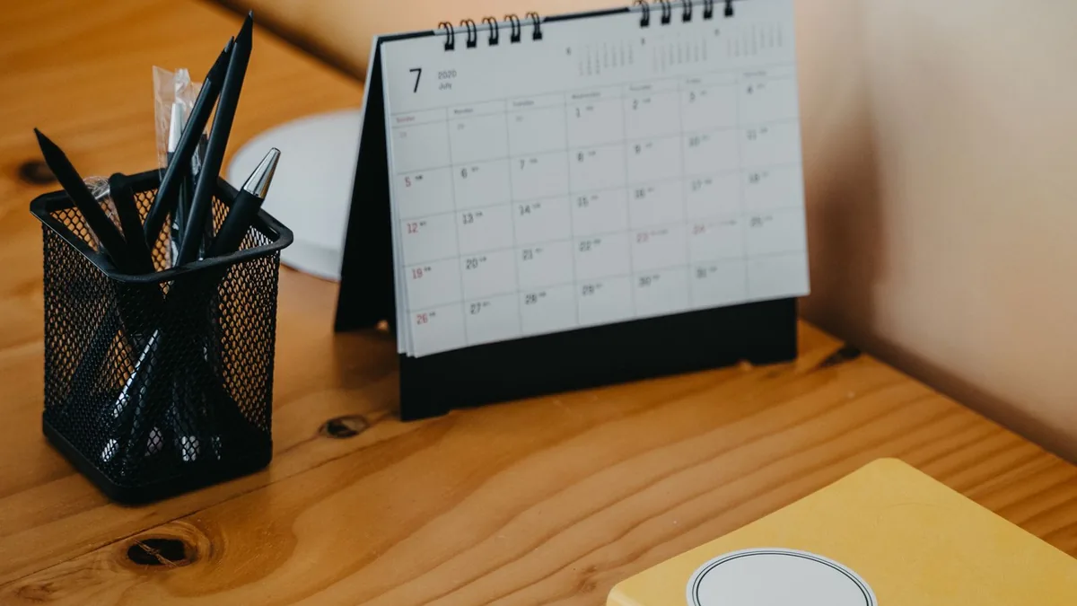 Mesa de trabalho organizada com calendário de mesa, caderno e porta-canetas
