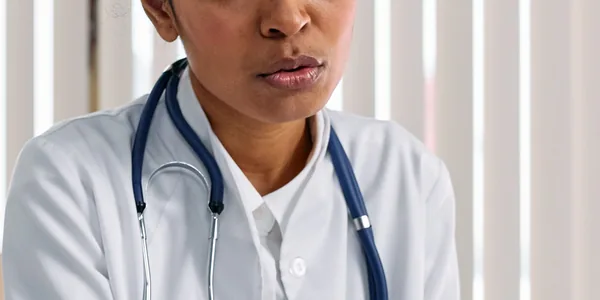 Médica de jaleco branco com estetoscópio conversando com um paciente sentado à mesa do consultório