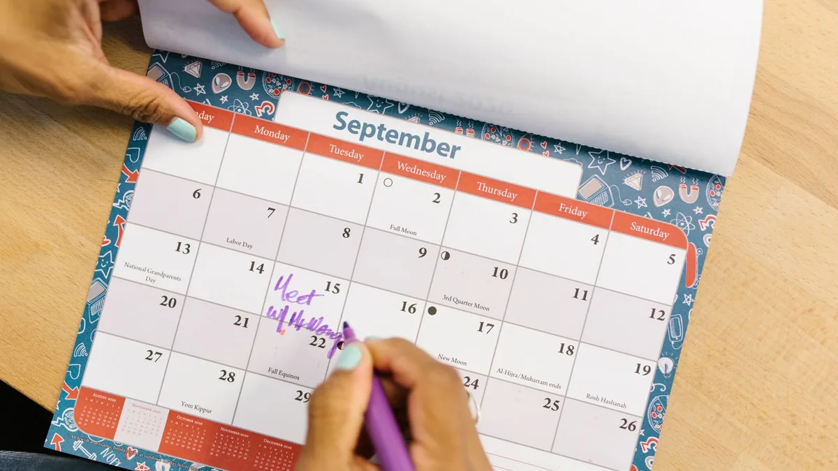 Mão marcando uma data no calendário de mesa aberto no mês de setembro