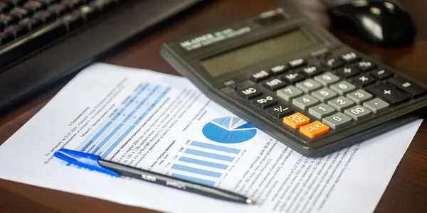 Mesa com calculadora, relatório financeiro e caneta para refazer a precificação com IBS e CBS