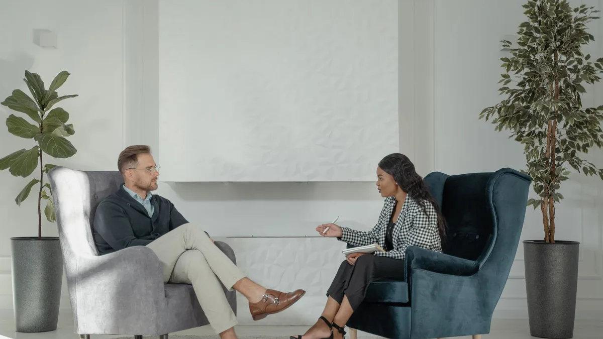 Psicóloga conversando com uma paciente em poltronas, num consultório com luz natural
