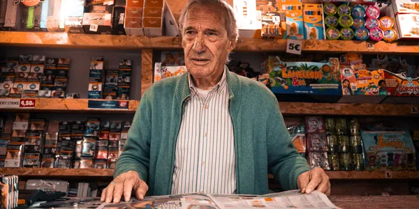 Comerciante idoso atrás do balcão de uma banca de revistas