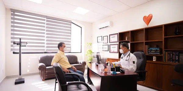 M&eacute;dico conversando com um paciente do outro lado da mesa em um consult&oacute;rio