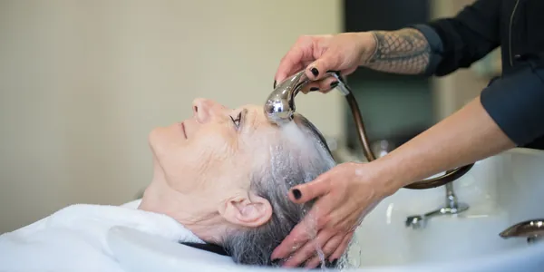 Cabeleireira lavando o cabelo de uma cliente na pia do sal&atilde;o