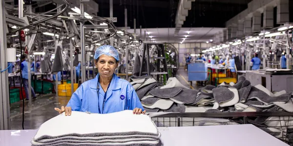 Trabalhadora dobrando peças em uma fábrica têxtil, cercada de máquinas