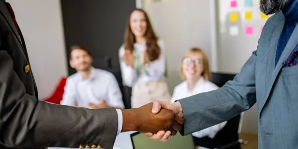 Aperto de mãos entre profissionais em escritório, representando a relação comercial entre empresas na Reforma Tributária