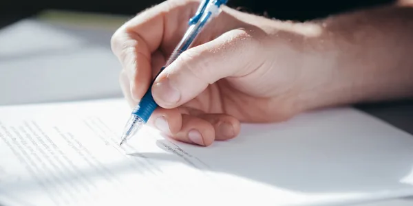Close de uma mão preenchendo um documento com caneta azul